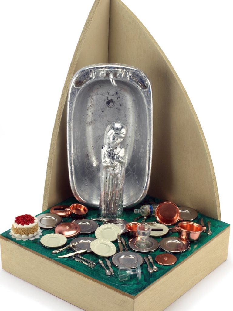 Image: Elaine Luther, Our Lady of Perpetual Dishes, 2013. 9 x 6 x 6 in. Wood, silver-leafed saint and doll bathtub, dollhouse miniature utensils, dishes, pots, water bottles, glasses, and cake. Acrylic paint and medium. A 6” x 6” wood base has two arching shapes at the back of it, topped by a tiny plastic dove. Just in front of the arching shapes is a doll bathtub, and in front of that, a saint figure. Both have been covered in silver leaf. At the feet of the saint are piles and piles of dishes: utensils, plates, pots and pans, a water bottle, wine glasses, and a perfect miniature cake with icing and cherries on top. The surface of the wood base is painted green as if the setting is a front yard. The dishes and pots are in a mess, spread all over the surface. The cake is in the corner, pristine and perfect. Courtesy of the artist.