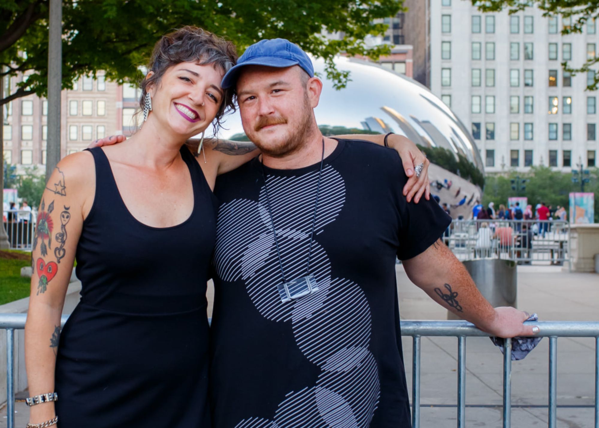 Image: kate and gurtie stand along a fence in Chicago's Grant Park, both wearing black t-shirts. The Bean (a.k.a. Cloud Gate) can be seen in the background. Photo by Sarah Elizabeth Larson, courtesy of the artists.