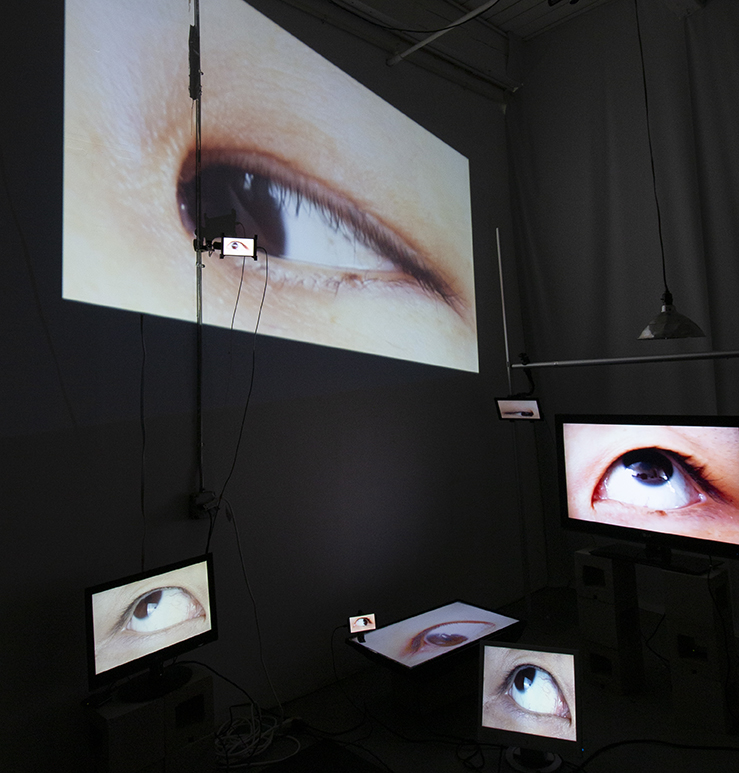 Image: The Audience, 2021.14 Channel video installation. Dimensions variable. Eight screens of various sizes display eyes in a dark room. Image courtesy of the artist.