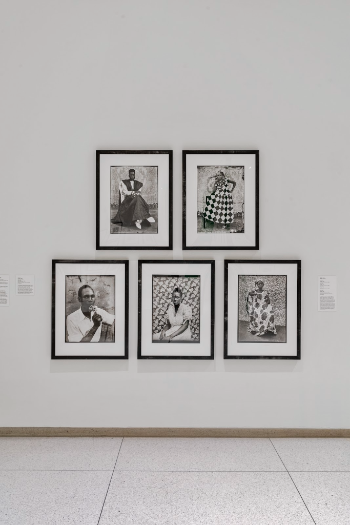 Image: A white gallery wall has five black and white studio images on it. Installation view, not all realisms: photography, Africa, and the long 1960s, Smart Museum of Art, The University of Chicago. Photo by Robert Chase Heishman. Seydou Keïta, Untitled #359 (1950–1955), Untitled #110 (1950–1955), Untitled #304 (1950–1952), Untitled #127 (1952–1958), and Self-Portrait (1949), printed 1995–1998, Gelatin silver prints. Collection of the Booth School of Business Art Collection.