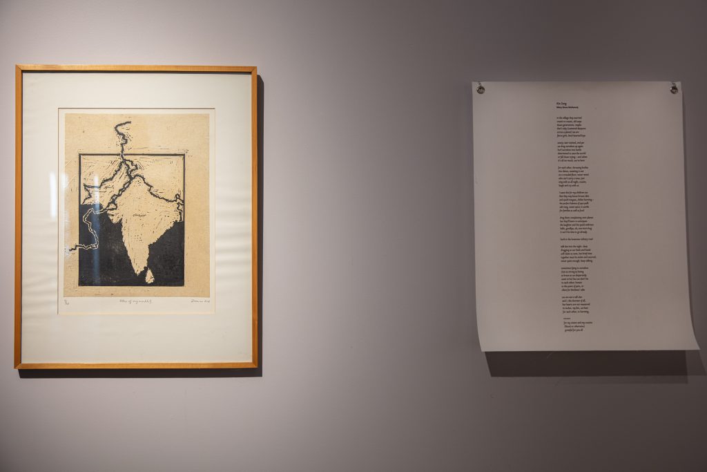 Image: An install photo from <i>Testimonies on Paper</i>. On the left is a print depicting a map of Pakistan and India from Zarina’s Atlas of My World portfolio. On the right on a piece of white paper is an accompanying poem, “Kin Song,” by Mary Anne Mohanraj. Courtesy of South Asia Institute.