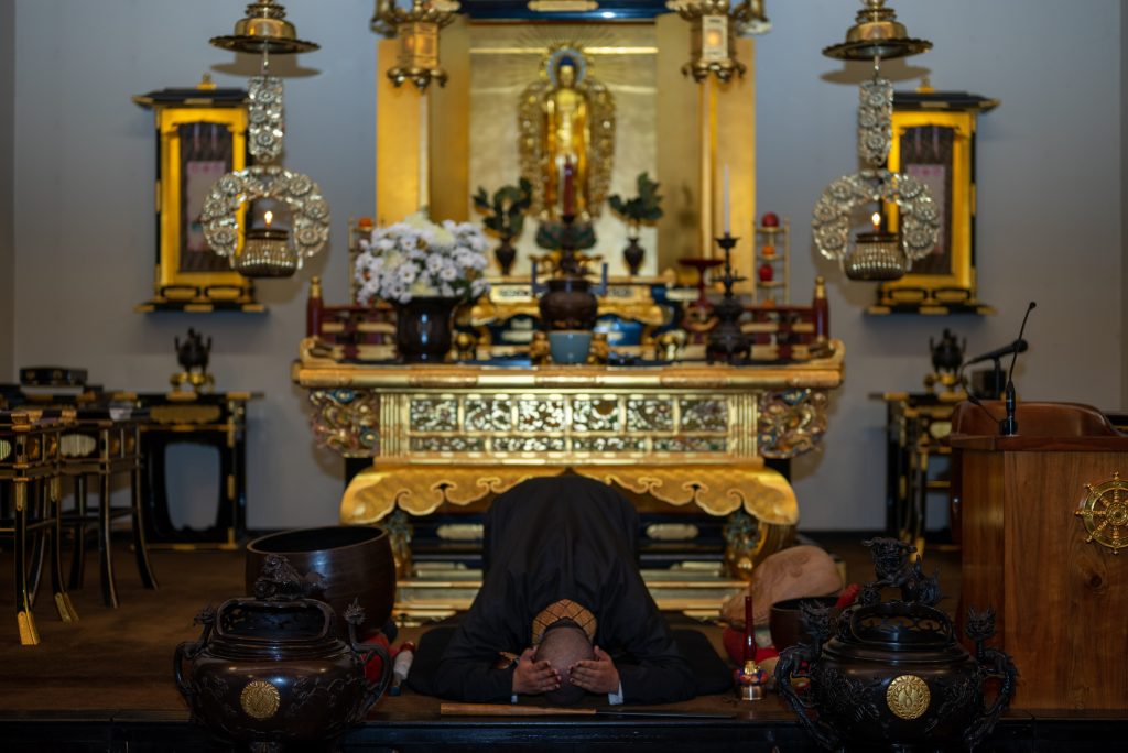 Image: Brown kneels with their hands on their head in front of a golden shrine. Photo by Tonal Simmons. 