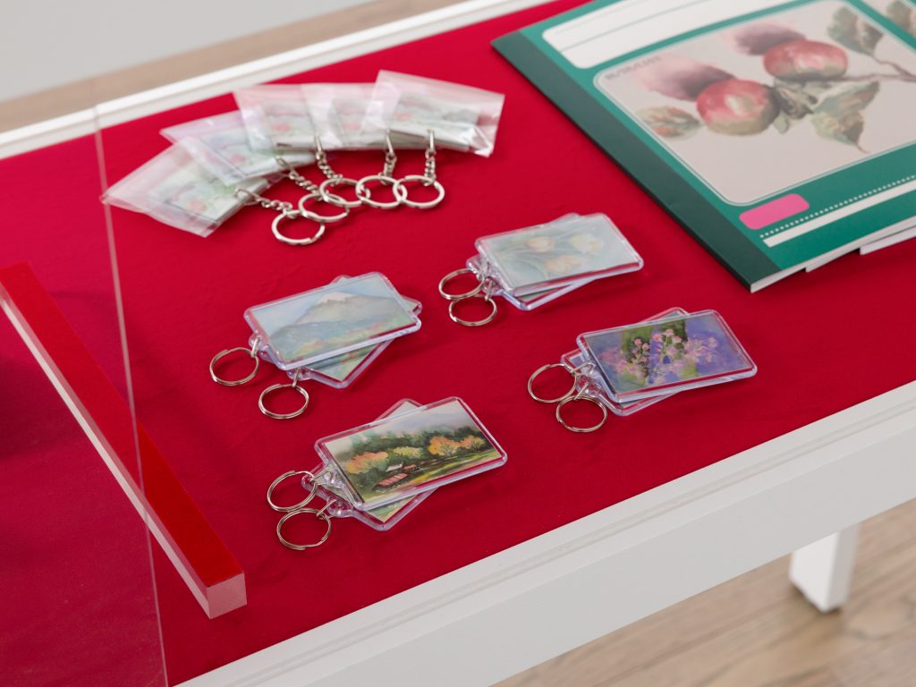 A detail image of Horibuchi's Showcase Vitrine 1 features keychains and notebooks branded with reproductions of Sayoko Yokoyama's watercolor paintings atop red velvet. 