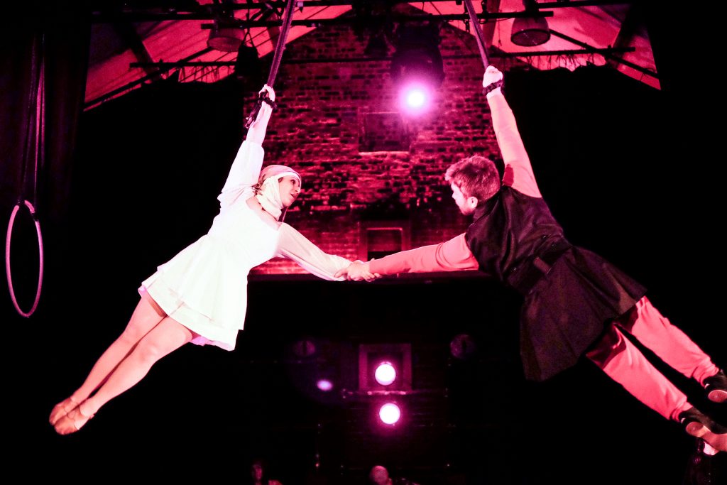 Image: Two Actors Gym performers soar through the air while holding hands during a performance. Image by Matthew C. Yee, courtesy of The Actors Gym.