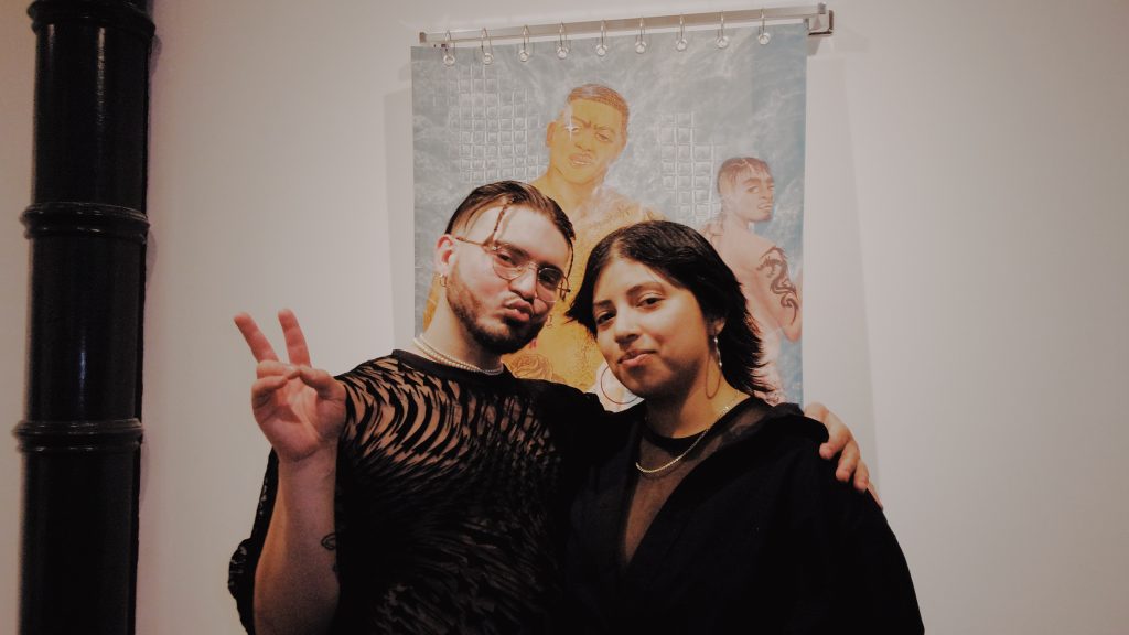 Image: Juan Aranga Palacios and Vani Aguilar posing in front of Palacios’ Al Vapor. Palacios holds up their hand in a peace sign. Photo by Luz Magdaleno Flores. 