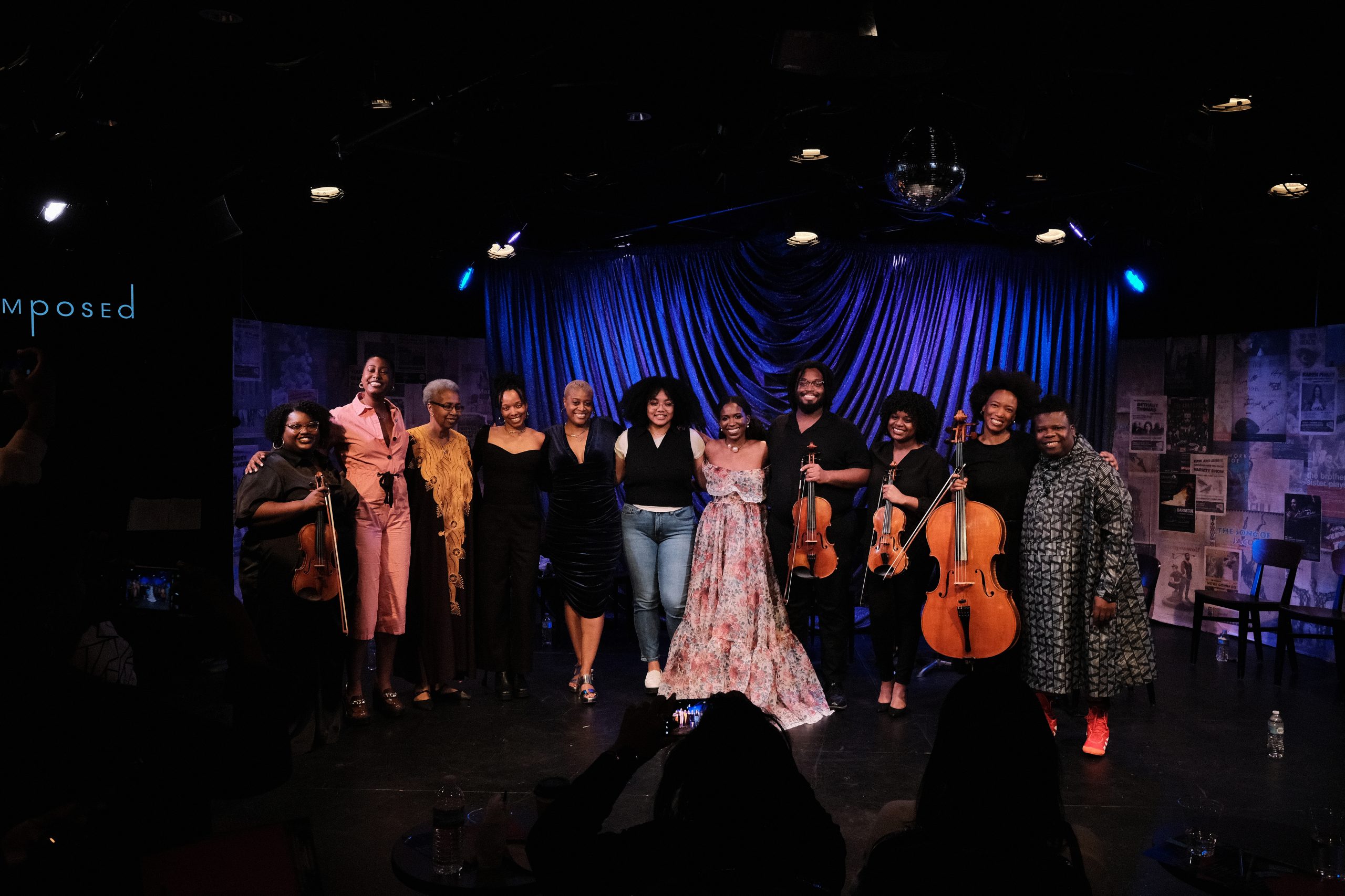 Image: A cast photo of D-Composition-Love Is...The eleven cast members stand in front of a deep blue velvet curtain. Photo by Sulyiman Stokes.