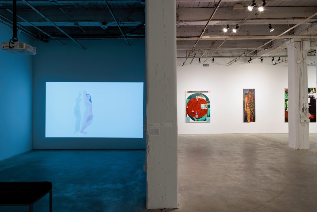 Image: Installation photo of Presence in the Pause: Interiority and its Radical Immanence. Danielle McKinney’s "Fly High" and "Calvary" paintings hang on the left with a light purple background.  Andrea Joyce Heimer's painting "I Fight Myself Over And Over And Over And Over And Over Again" is displayed in the middle. The exhibition text is displayed on the right. Image courtesy of Bemis Center For Contemporary Arts.