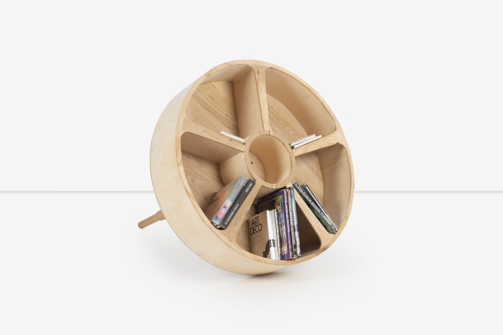 Image: Norman Teague, Self Portrait, 2022. A wooden sculpture/bookshelf that resembles the shape of a wheel. In the center of the 'wheel' form are books. and Photo by Converso Modern.