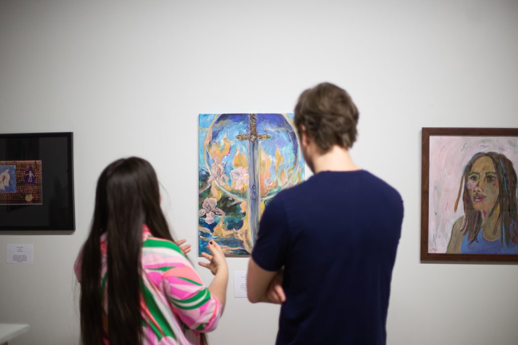 Image: Two audience members discuss the painting in front of them. The painting depicts a burning sword and is by PGOBA artist Brenda Pagan. Photo by Alexa Cary. 