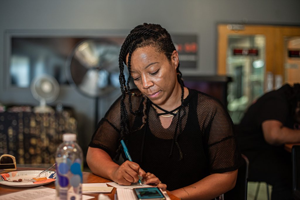 Image: Tempestt Hazel sits in the audience of the event and writes her feedback for the participating artists. Photo by Alexa Cary.