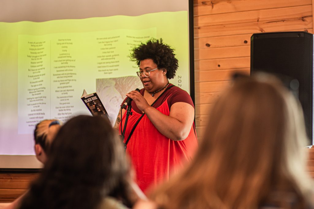 Image: Hannah Offutt stands in front of an audience while reading their work. Photo by Alexa Cary.