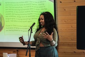 Image: Autumn Angelize speaks into a mic in front of an audience at CANJE Session 1: The Art of Critique.