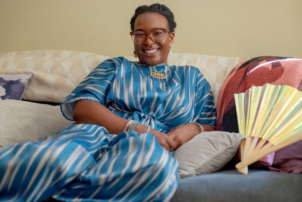 Image: Portrait of Jade T. Perry smiling while sitting on a couch. Photograph by Tonal Simmons. 