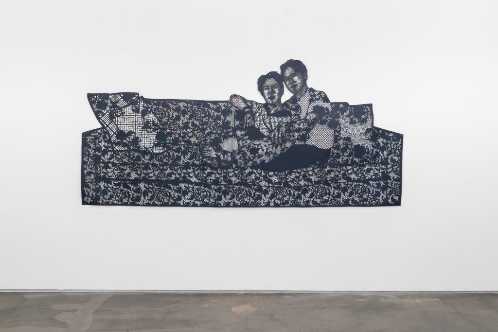 Image: The work of love becomes its own reasons, 2023 52 x 112 in 132.1 x 284.5 cm. The work features a detailed lattice of cut paper to illustrate two people holding each other on a floral-patterned couch. Image courtesy of Monique Meloche gallery. 