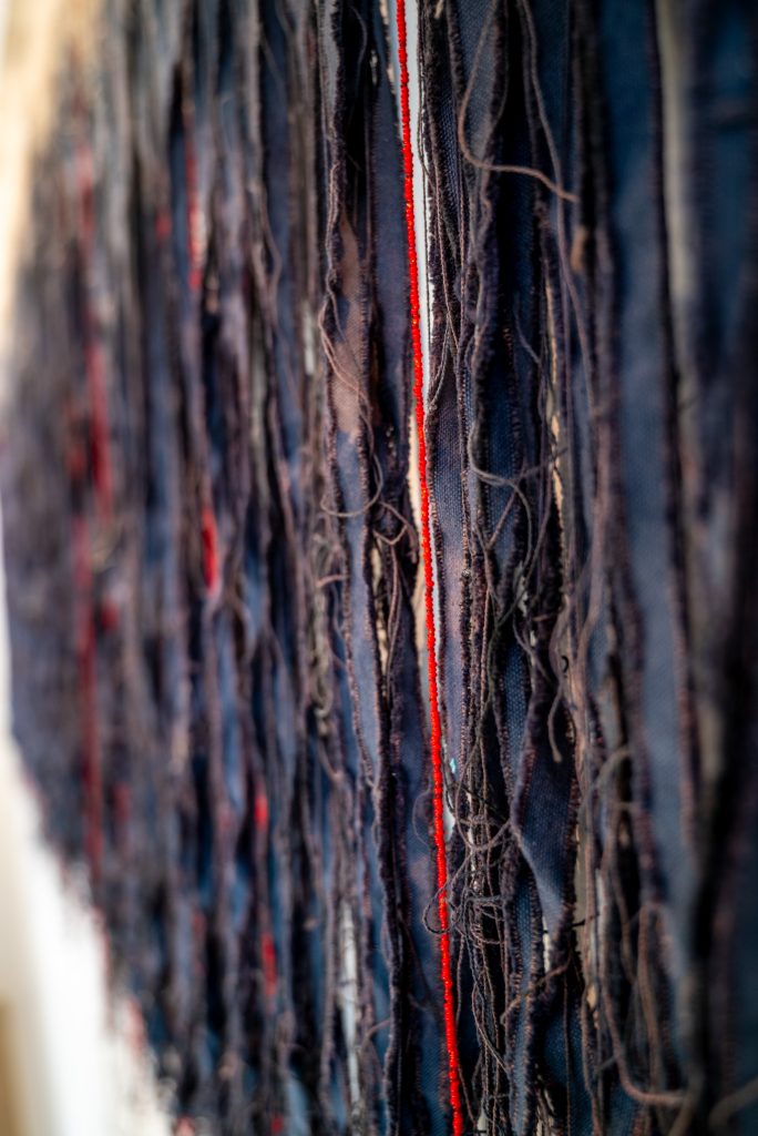 Image: Close-up of Chelsea Bighorn's Black Fringe. Red, blue, an purple threads mix with the fringing of cloth. Photograph by Tonal Simmons. 