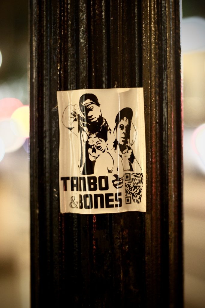 Image: A street pole con un sticker de la produccion Tambo & Bones. Foto x Luz Magdaleno Flores.