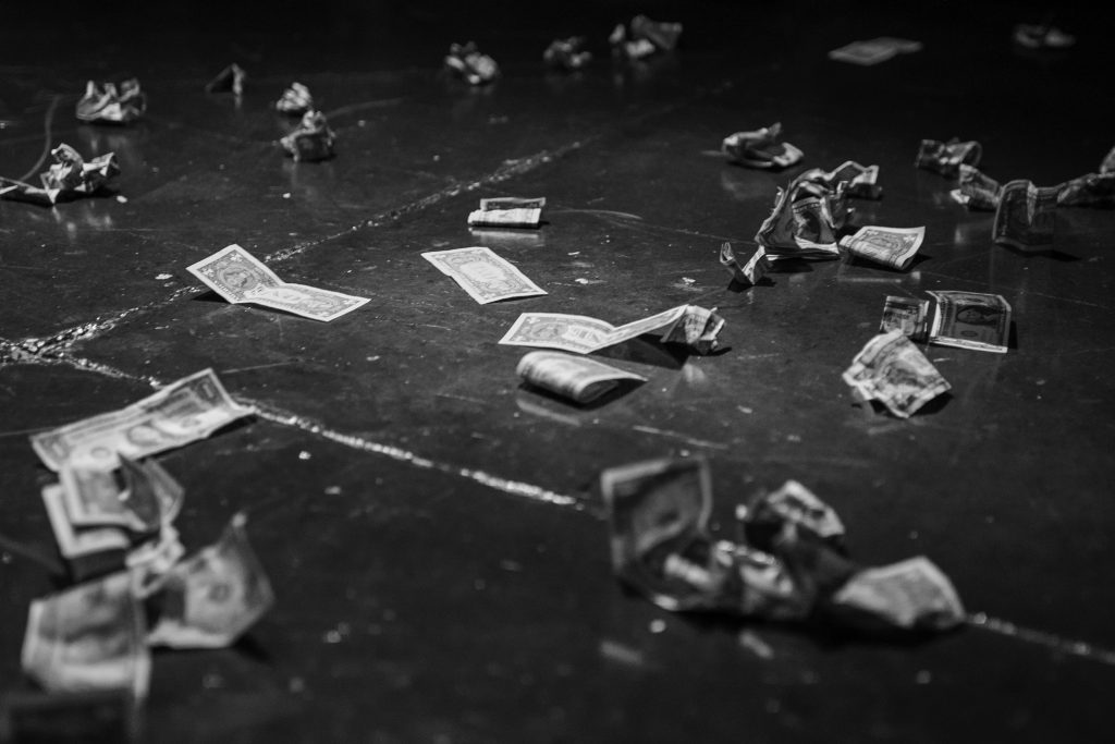 Image: Black and white image of stray tips on the dance floor at Obscura at Simone’s, 2022. Some of the bills are totally crumpled, while a few in the center of the image remain flat on the floor or have only one fold in them. Photo by Erica McKeehen.