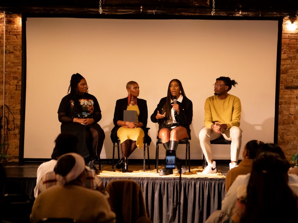 Image: Redmond, Brunson, and Rudd-Ridge on a panel at the "A Long Way From Holmes" film screening. There are some audience members upper bodies in the foreground. Behind the panelists is a white screen. Photo by Nick Moody
