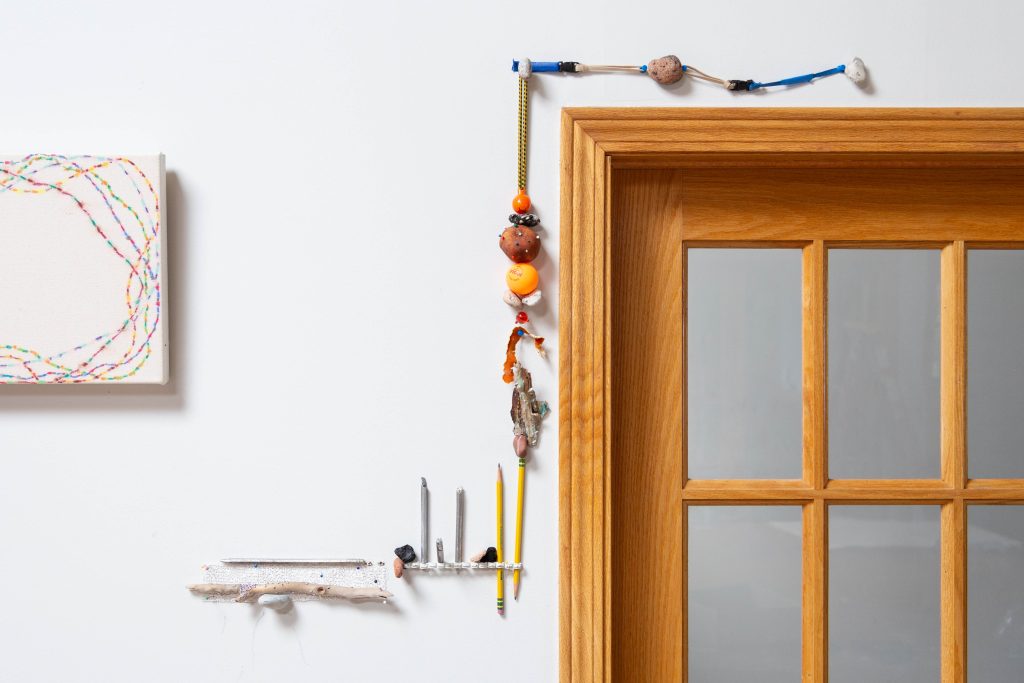 Photography: Series of small objects (orange peels, small sticks, little stones) aligned and creating a frame-like line around the top left corner of a wooden door.