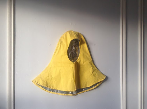 Photography: Yellow hood made of waterproof material, hung on a white wall.