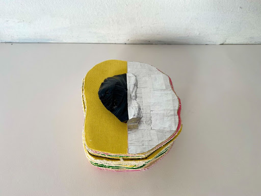 Photography: Multi Layered colorful form with a smaller black object, half of it is painted in silver on the top surface shape, the other part of the surface is painted in yellow.