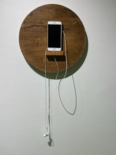 Photography: White iPhone with white headphones, hanging on the wall on a round shelf made of wood that creates a circumference around the cell phone.