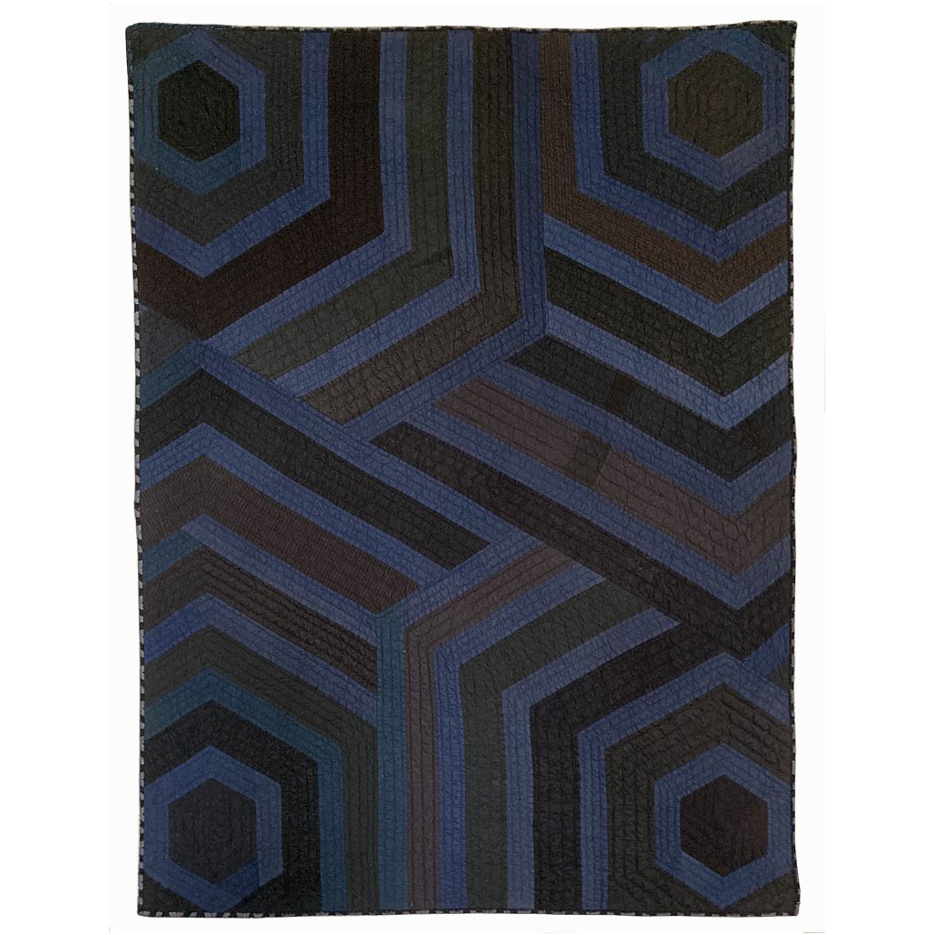 Photography: Quilt made with vintage Japanese cotton dyed indigo and geometric lines with other shades of dark and light brown. Parts of four hexagonal shapes can be perceived.
