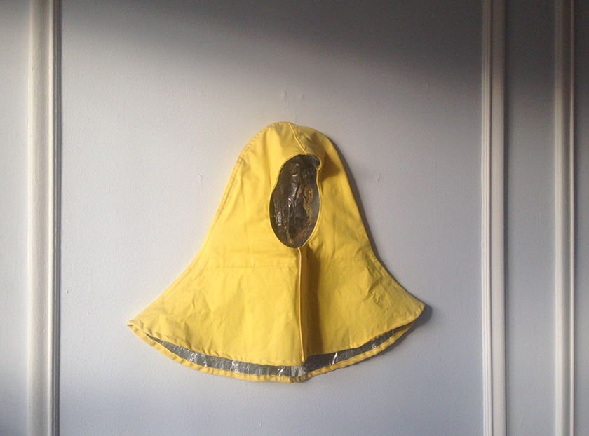 Fotografía: Capucha amarilla hecha con una tela para la lluvia colgada sobre una pared blanca