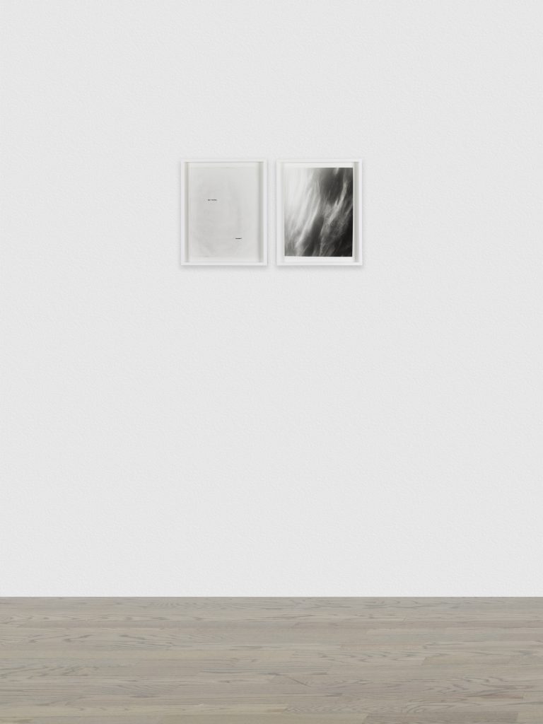 Image: Brittany Nelson, Starbear and Mars Clouds 3, 2021 Gelatin silver print. A white gallery wall with two framed art pieces on it. The left piece is mostly blank, with a greyish smudge and two little black scratches on it. The right image is a fluid image of Mars's clouds in black, white, and grey. Image courtesy of Patron Gallery. 