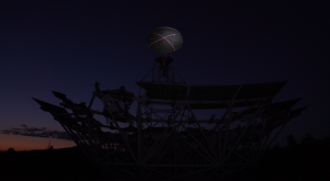 Image: Brittany Nelson, still frame from "I can't make you love me," single channel video, 2024. The Allen telescope, a many-faceted structure, is silhouetted in the foreground, much of its detail is hard to see. Behind it, is a barely lit horizon. Image courtesy of Patron Gallery.