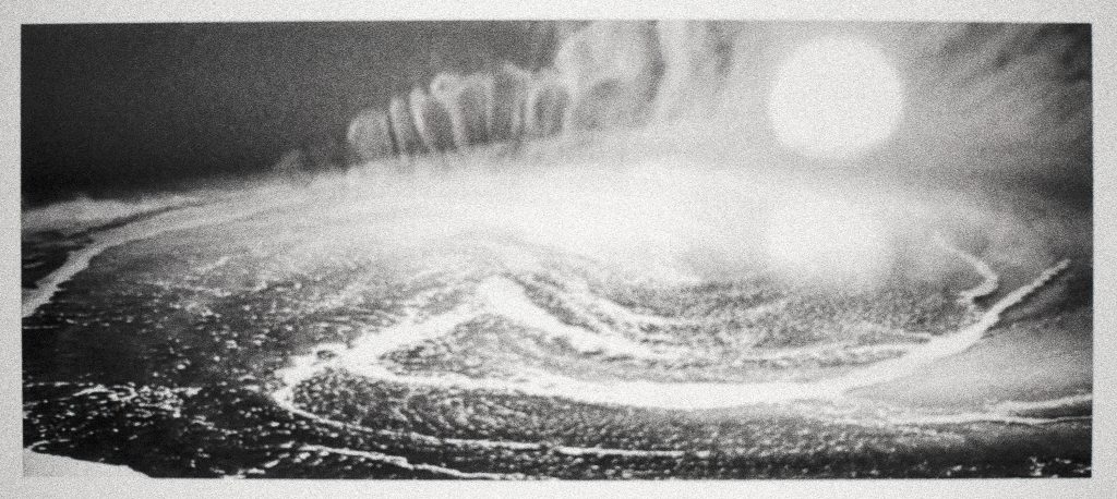 Image: Brittany Nelson, Solaris Ocean #1, 2023, unique silver gelatin print. A greyscale still from "Solaris" in which an ocean swirls, steam rises off of it. Behind the steam is a massive white sphere. Image courtesy of Patron Gallery. 