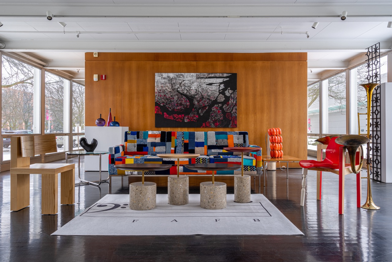 Image: Installation view of A Love Supreme: McCormick House Reimagined. Small tables made of laminated and bent birch, vegetan leather and cowhide; sprayed metal sit in the center of a room surrounded by a variety of furniture including a colorful, patchwork couch and a red plastic chair. Photo by Siegfried Mueller, courtesy of the McCormick House.