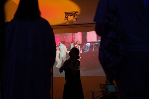 Image: A black silhouette of a person is captured in front of a projected film scene that shows people running towards a red classic car during Dark and Hot at Comfort Station. Photo by Jonas Mueller-Alheim, 2023.