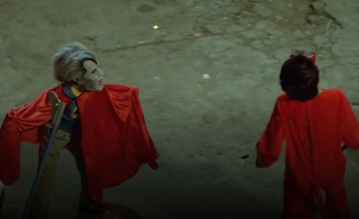 Image: A still image of Pura Sangre (1982). To figures wearing red stand in the foreground. The figure on the right appears to be a vampire.