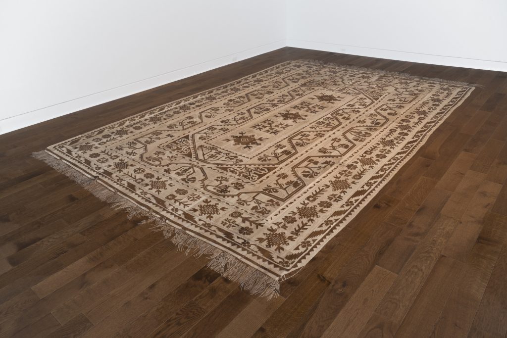 Image: Selva Aparicio, Childhood Memories, 2023-24, artist’s mother's rug carved into oak floor. Courtesy of the artist. In Memory Of, installation view, DePaul Art Museum. Photo by Bob.