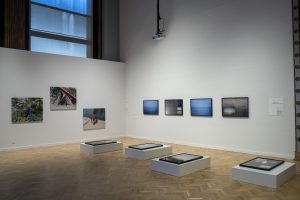 Image: Installation view in a corner of the Chicago Cultural Center. On the left wall of the image are three of Marion Poussier’s photographs from On est là (2021), and the adjacent wall are four of zakkiyyah najeebah dumas o’neal’s photographs of Lake Michigan, with four more mounted on platforms on the ground. Poussier’s photographs are three scenes from beside the Canal St. Denis, and dumas o’neal’s are close-ups of light hitting the lake in varying hues. Courtesy of Villa Albertine.