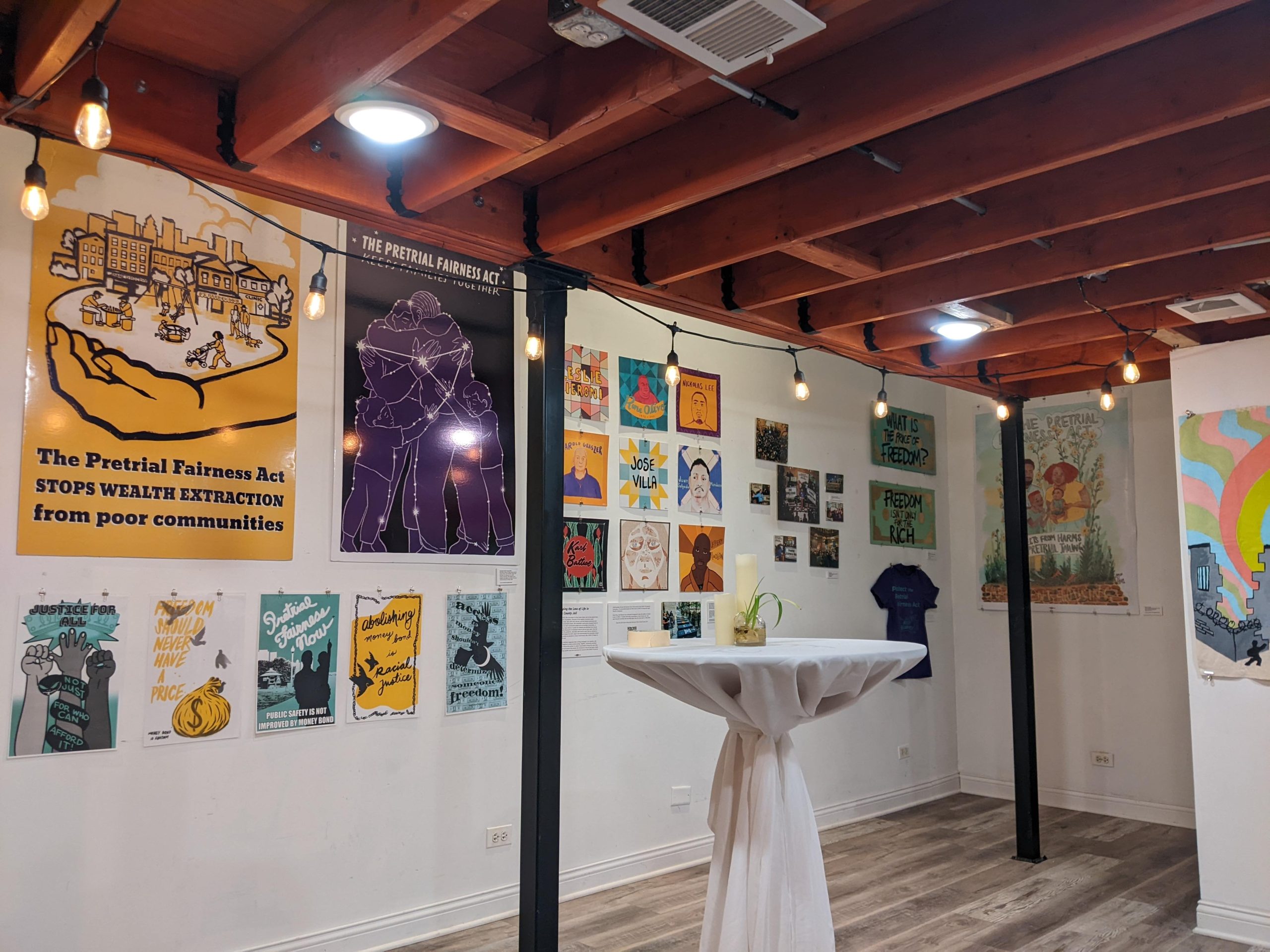 Image: Art In Action Exhibition wall at the Dragonfly Gallery. Photo features artwork by Just Seeds Cooperative and the For the People Artist Collective. The ceilings are orange wood rafters. Photo courtesy of the author.