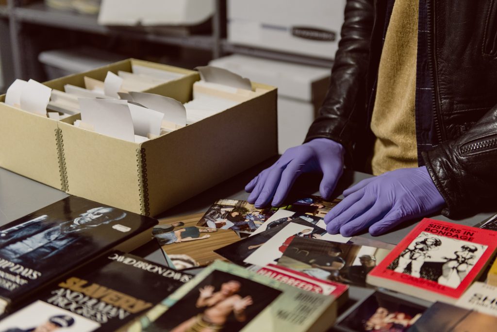 Image: CA+AP artist Aay Preston-Myint looks through photographs from the collection at the Leather Archives & Museum. Photo by Ryan Edmund Thiel.