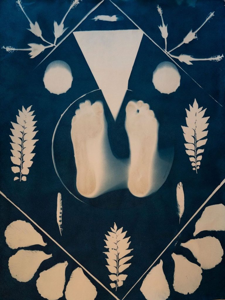 Image: Tarrah Krajnak, For Maria, from Ayni, Offerings for my Sister series, 2022. Cyanotype. Collection of the Museum of Contemporary Photography. On a cyanotype blue, a symmetrical arrangement of two feet in the center, with leaved plant stems on either side and one underneath. Diagonal bottom from the feet are two slightly different feathers, blade side inwards. Further, in the corners, are four flower petals on either side, separated from the rest of the image by a white line, running from the bottom center at a 45 degree angle towards the sides. The feet are wedged by a white triangle cutout with a circle cutout on either side of its bottom point. In the top corners of the image are three flowers with their pistils pointed outward.  Image courtesy of MoCP.