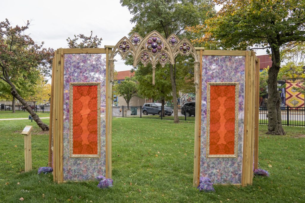 Image: Earthen, 2022 by The Black Bloom Project (Jade Williams and Cristabel Martinez), installed as part of Finding Ceremony—Tiffany Johnson's project for her 2022 Anchor Curatorial Residency at Austin Town Hall. The installation is a symmetrical structure with stained-glass-like purple and orange sections on the left and right. The top is ornate purple and a bronze-like color in shapes that mimic gothic windows. Image courtesy of Tiffany Johnson. Photographer: Vanessa Lara/ Colectivo Multipolar.