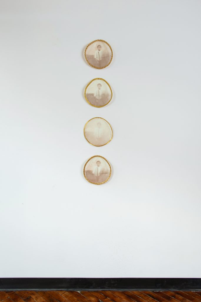 Image: Offerings by Thương Hoài Trần hangs on a gray wall. The piece is made up of four screen prints with gold trim hung vertically. Photo by Khalid Ibrahim.