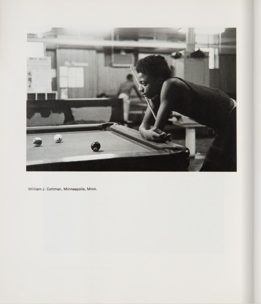 Image: A photograph, taken by William Cottman, depict a young man leaning upon a pool table looking at the game in front of him. Three balls are positioned in frame on the table. Behind him is a bar and other tables. William Cottman's photograph featured in the third edition of the Black Photographers' Annual (1976). Scan and photo courtesy of writer.