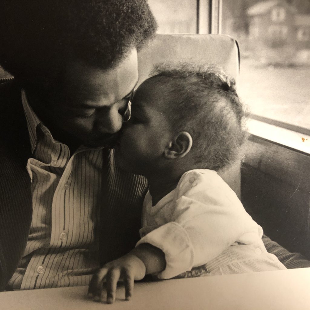 Image: A baby leans to kiss a man on the cheek. The man and the baby are captured in a close cropped shot. They sit in what resembles a diner booth. William Cottman with Kenna Cottman. Photo courtesy of writer.