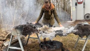 Image: Debbie Christensen, a member of Rust Belt Fibershed, tanning local hides over a fire outdoors. Photo Courtesy of Corinne Wiseman.