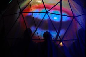 Image: Image of a mouth is projected onto a geometric dome. Silhouettes of audience members are visible in front of the projection. Photo by Michael Wellvang. Image courtesy of Anna Johnson.