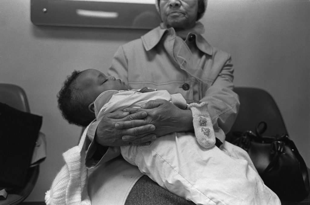 Image: A seated woman holds a sleeping baby. Evelyn Cottman holds Kenna Cottman, photographed by William Cottman.