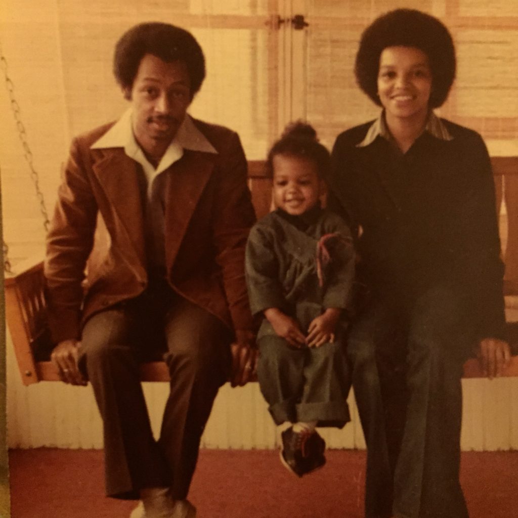 Image: A man and a woman sit smiling on a porch swing, a little girl sits between them, she's also smiling. William, Beverly, and Kenna Cottman at their home in South Minneapolis. Photo courtesy of writer. 