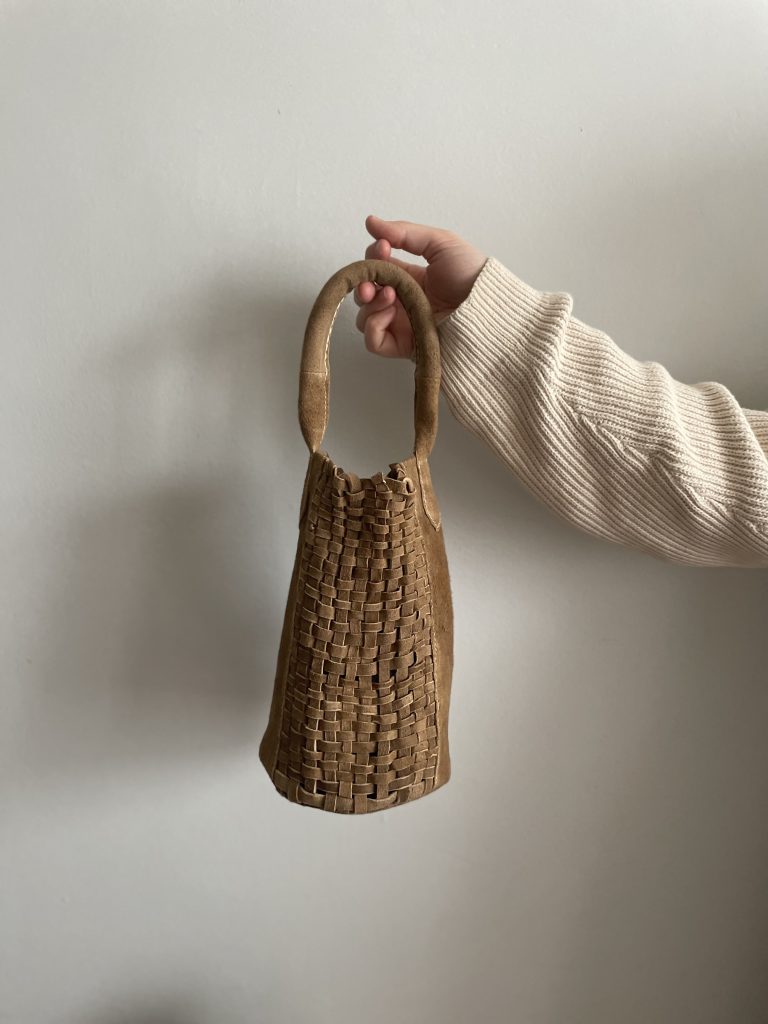 Image: A hand holding a leather bag against a white background. One Year One Outfit participant Courtney Phillips' Woven Buckskin Leather Bag. Photo Courtesy of Courtney Phillips.