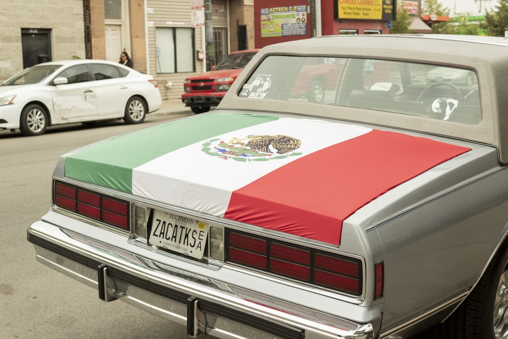 Imagen: La cajuela de un carro classico color gris es decorado con una bandera Mexicana. Las placas len ZACATKS, un homenaje a el estado de Zacatecas en México. Foto x Cobalto es azul, 2023.