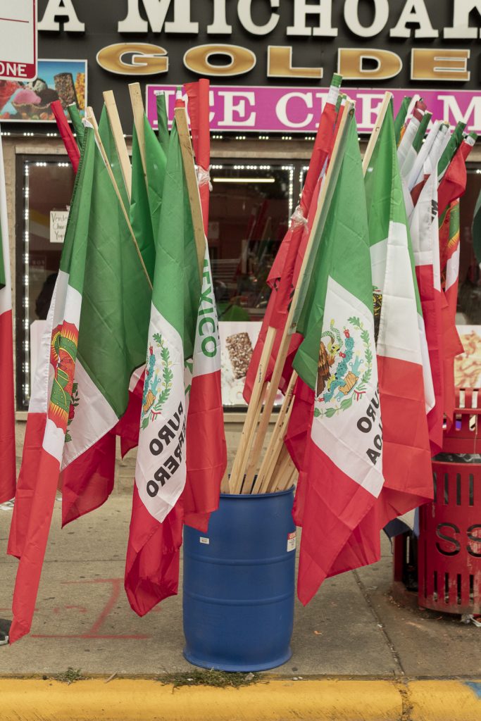 Imagen: Un bote azul detiene mas de diez banderas grandes Mexicanas en frente de La Michoacana en la calle 26 en Chicago. Foto x Cobalto es azul, 2023.